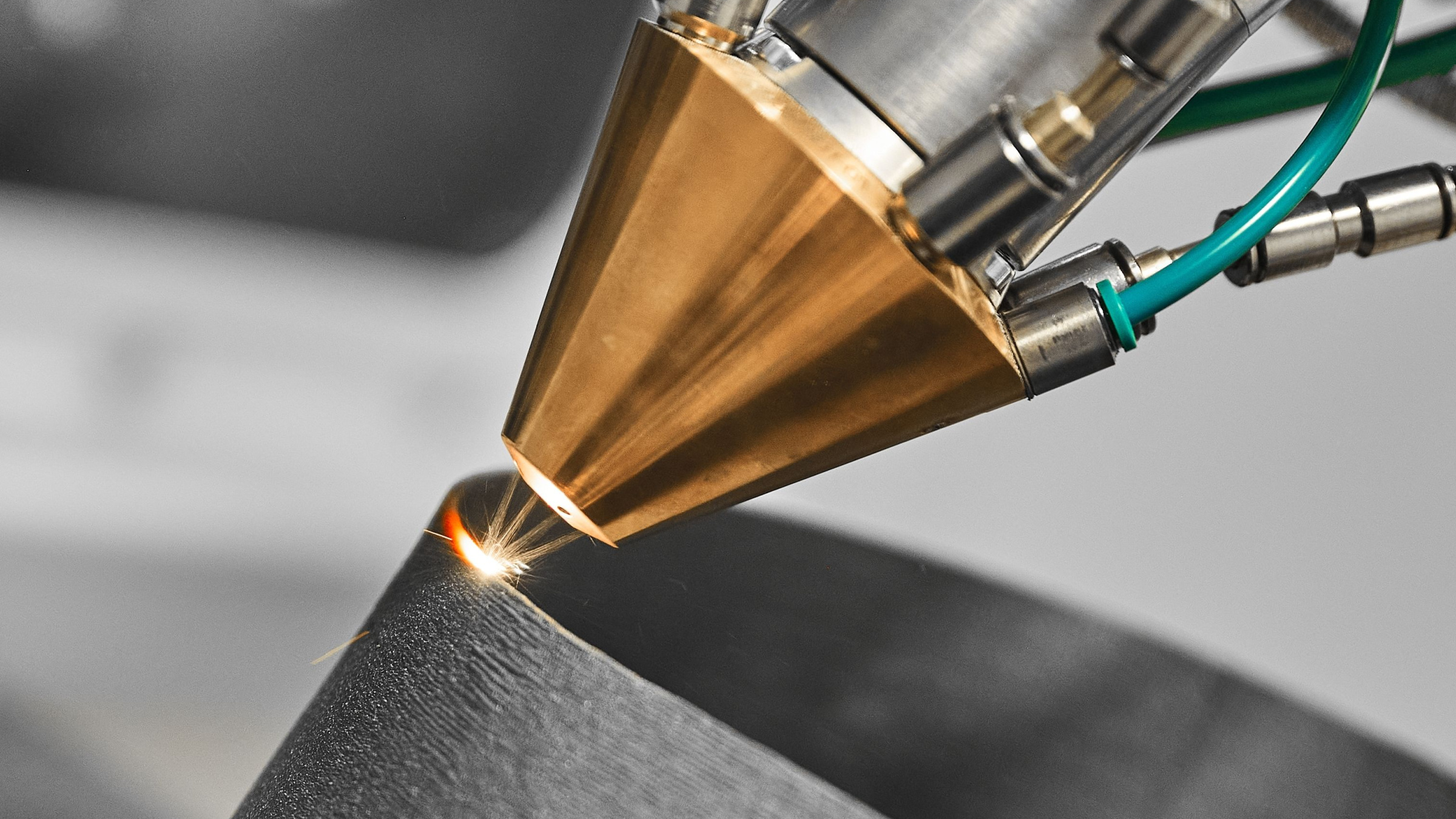 Close-up of a directed energy deposition print head: a laser melts metal powder blown onto a curved steel part, throwing sparks